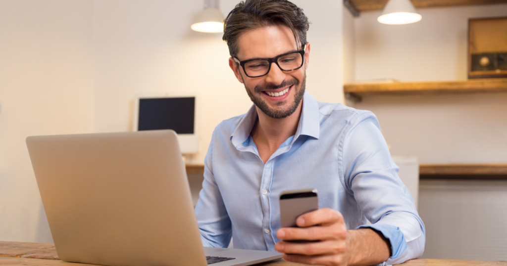 Man smiling at phone with laptop open